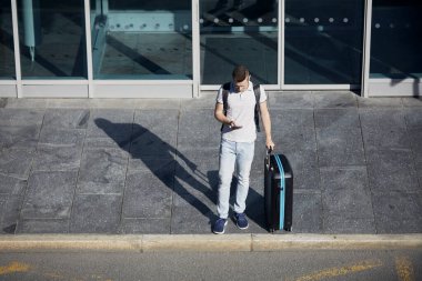 Akıllı telefonda mobil uygulama kullanan bir adam. Valizli yolcu şehir caddesinde bekliyor.. 