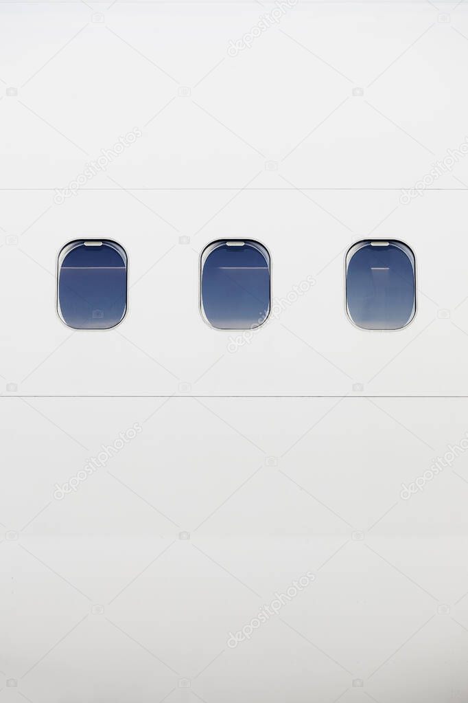 Three windows on fuselage of white airplane. Vertical image of plane with copy space