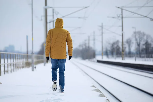 Rear view of loneliness person in warm clothing. Man leaves train station against snowy landscape