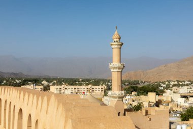 Nizwa Kalesi 'nin duvarları ve El Kala Camii' nin Nizwa, Umman 'da gün ışığıyla aydınlanan dağlara bakan görüntüsü. Tarihi mimari, sıcak ışık ve geleneksel Orta Doğu atmosferi..