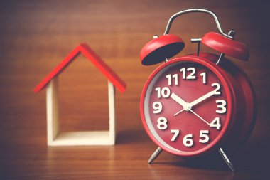 clock and miniature house on wooden background, copy space.