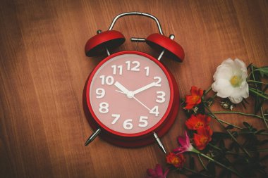 Ahşap arka planda kırmızı saat ve çiçekler