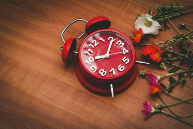 Ahşap arka planda kırmızı saat ve çiçekler