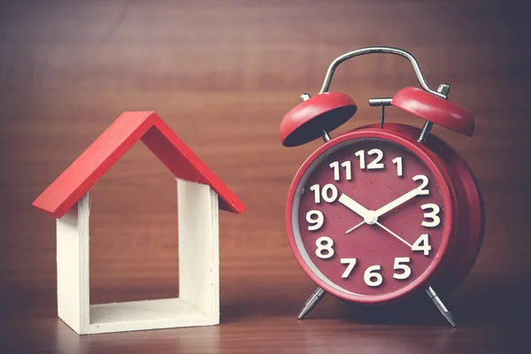 clock and miniature house on wooden background, copy space.