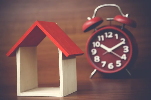 clock and miniature house on wooden background, copy space.