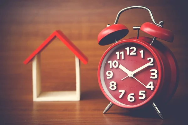 clock and miniature house on wooden background, copy space.