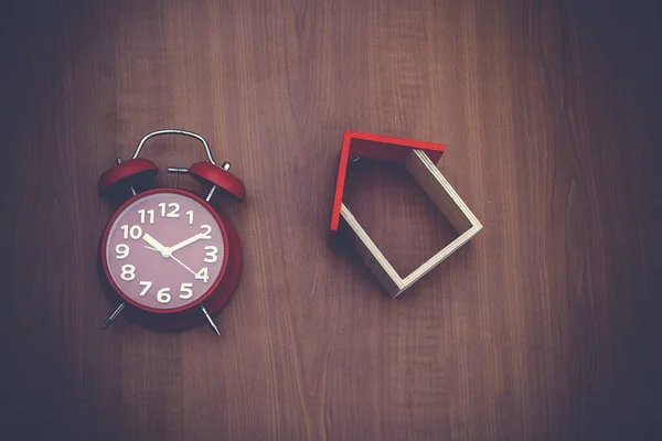 Ahşap arka planda ahşap oyuncak ev ve kırmızı saat. Boşluğu kopyala