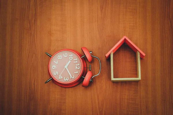 Ahşap arka planda ahşap oyuncak ev ve kırmızı saat. Boşluğu kopyala