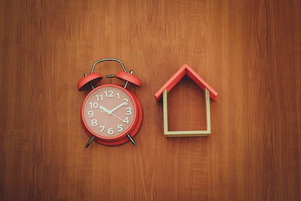 Ahşap arka planda ahşap oyuncak ev ve kırmızı saat. Boşluğu kopyala