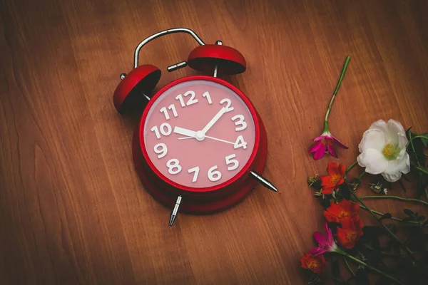 Ahşap arka planda kırmızı saat ve çiçekler