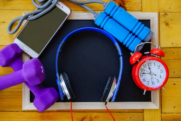 Spor, spor konsepti. Koşan spor ayakkabılar, su şişesi, kulaklıklar, dambıllar, akıllı telefon, ahşap arka planda fotokopi alanı