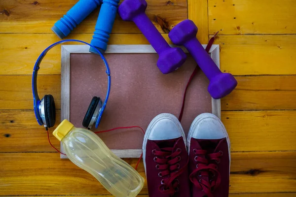 Spor, spor konsepti. Koşan spor ayakkabılar, su şişesi, kulaklıklar, dambıllar, akıllı telefon, ahşap arka planda fotokopi alanı
