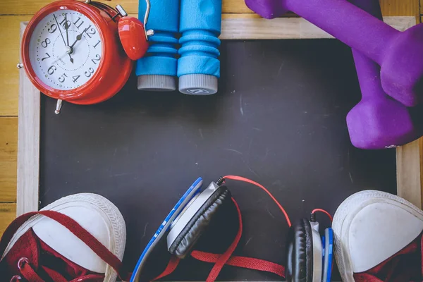 Spor, spor konsepti. Koşan spor ayakkabılar, su şişesi, kulaklıklar, dambıllar, akıllı telefon, ahşap arka planda fotokopi alanı