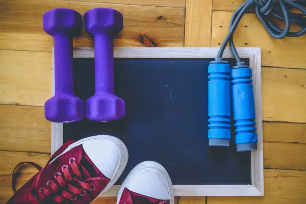 Spor, spor konsepti. Koşan spor ayakkabılar, su şişesi, kulaklıklar, dambıllar, akıllı telefon, ahşap arka planda fotokopi alanı