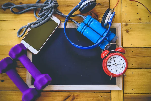 Spor, spor konsepti. Koşan spor ayakkabılar, su şişesi, kulaklıklar, dambıllar, akıllı telefon, ahşap arka planda fotokopi alanı