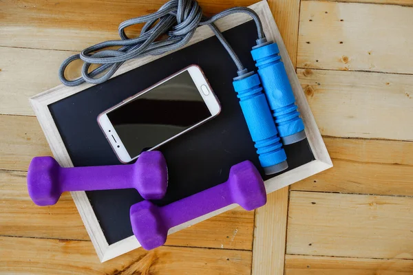 Spor, spor konsepti. Koşan spor ayakkabılar, su şişesi, kulaklıklar, dambıllar, akıllı telefon, ahşap arka planda fotokopi alanı