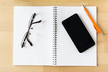 Ahşap Ofis Masası, not defteri, akıllı telefon, kalem ve gözlük