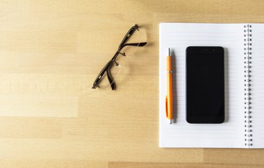 Ahşap Ofis Masası, not defteri, akıllı telefon, kalem ve gözlük