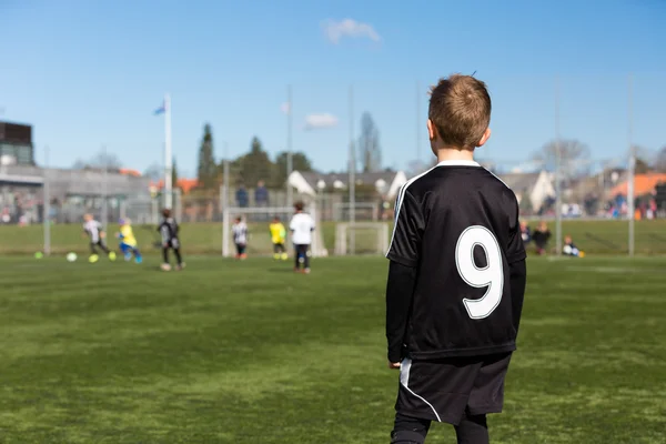 Menino assistindo jogo de futebol juvenil — Fotografia de Stock