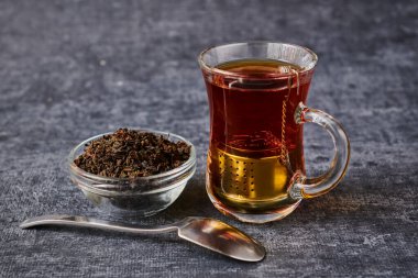 Çay fincanı manzarası elek yanında bira ve çay kaşığı ile gri arka planda.
