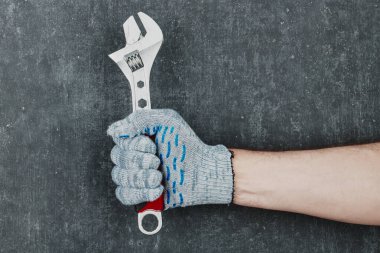 Gri arka planda ayarlanabilir İngiliz anahtarı tutan adamın eli eldivenli.