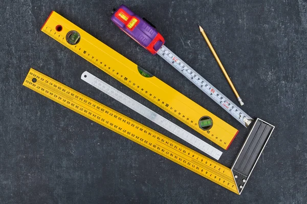 Ruler, tape measure, construction level and pencil on grey background, close-up view from above