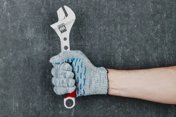 Man\'s hand holding an adjustable spanner wrench on gray background, man\'s hand in gloves