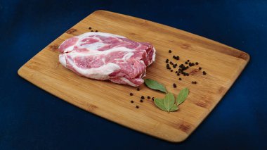 Tahta kesme tahtasındaki domuz boynundan bir parça. Et, defne yaprağı ve karabiber. Mavi arkaplan