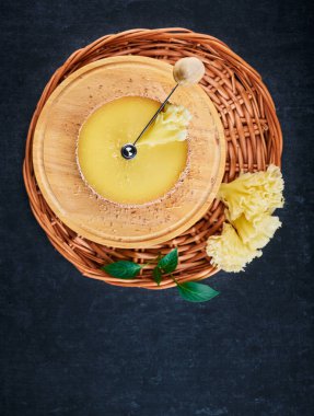 Tete de Moine cheese on the device cheese cutter and on a braided basket on a dark background, shallow depth of sharpness