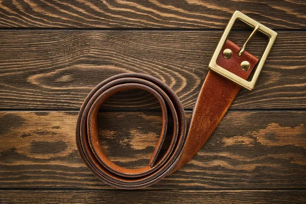 Mens wide brown belt made of genuine leather with a buckle for jeans on a wooden background, genuine leather