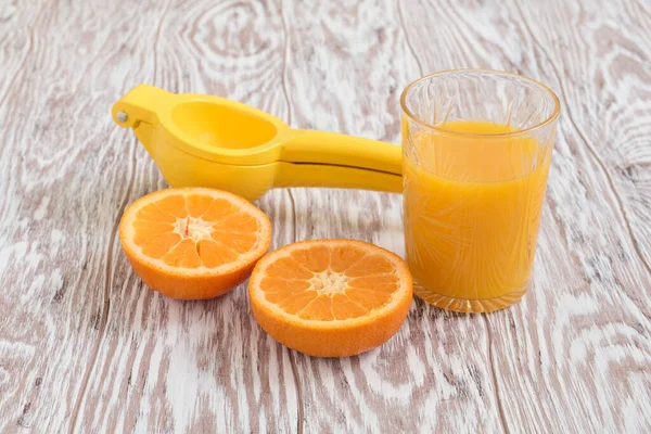 Glass of freshly squeezed juice, halves of a ripe tangerine, and a hand juicer lie on a wooden table, close up, shallow depth of field