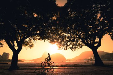 Sabahın erken saatlerinde Rio de Janeiro 'da Güzel Sıcak Gündoğumu sırasında Horizon' da Sugarloaf Dağı 'nda bisiklet süren bir kadının silueti.