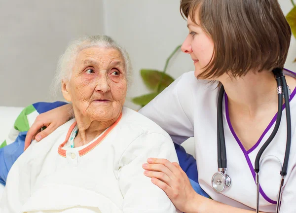 Junge Krankenschwester pflegt eine alte Dame, die im Bett liegt — Stockfoto