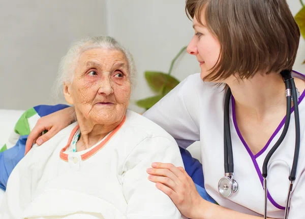 Jeune infirmière soignant une vieille dame couchée au lit — Photo