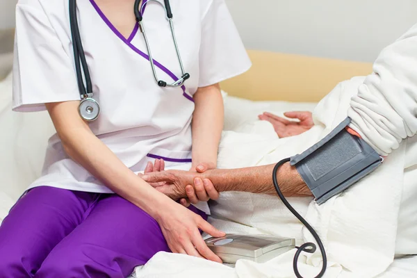 Young nurse caregiving an old lady lying in bed — Stock Photo, Image