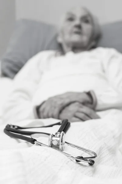 Пожилая женщина лежит больная в постели со стеоскопом — стоковое фото