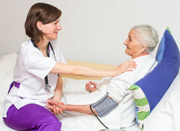 Junge Krankenschwester pflegt eine alte Dame, die im Bett liegt — Stockfoto