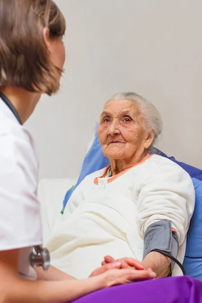 Ung sjuksköterska omvårdnad en gammal dam i sängen — Stockfoto