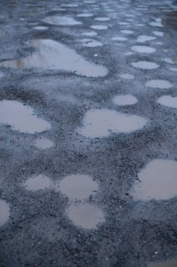 Bulanık su birikintileri engebeli bir çakıl yüzeyi, bulutlu gökyüzünü yansıtıyor.