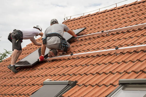 Two engineers on the house roof assemble photovoltaic panel.