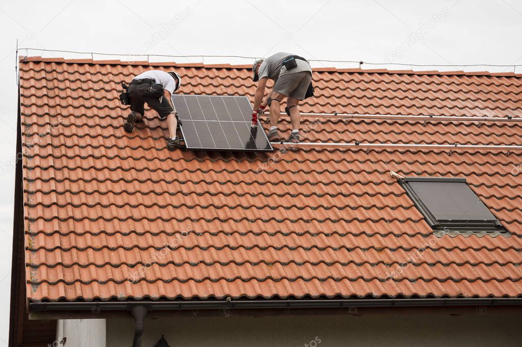 Two engineers on the house roof assemble photovoltaic panel.