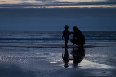 Karanlık çöktükten sonra sahilde oynayan bir adam ve çocuğun silueti.