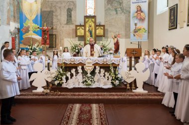 TYMOWA, POLAND - 22 Mayıs 2022 Kilisedeki ilk Kutsal Komünyon kutlamaları sırasında bir rahip ve çocuklar