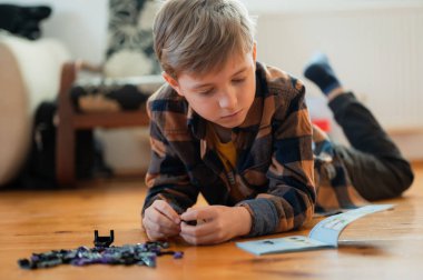 Genç çocuk talimatlara bakarak blokları topluyor.