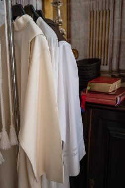 Fiew papazının sürpüsü, askıda ayin kıyafetleri, arka planda kutsal kitap.