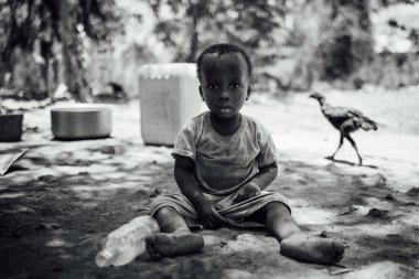 MICHAMVI KAE, ZANZIBAR - 17 Ekim 2025: Açık havada oturan küçük bir çocuğun monokrom portresi, arka planda bir tavuk ve doğal, samimi bir atmosfer, Afrika, etnik köken, Afrika