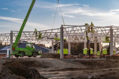 Profesyonel inşaat ekibi, bir endüstriyel yapı projesi için beyaz çelik çatı kirişleri yerleştirmek için teleskopik denetim ve hava asansörleri kullanıyor..