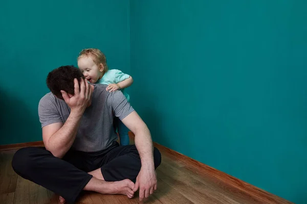 Child toddler screams in the ear of the father sitting on the floor in an empty dark room. Mental health or family problems concept. Copy space