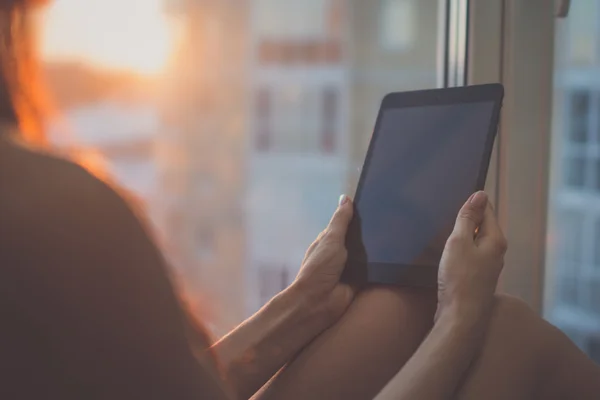 Femme assise à côté de la fenêtre en utilisant la tablette — Photo