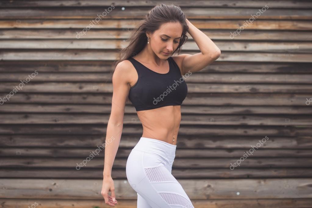 Young athletic woman in sportswear posing in studio against black  background. Ideal female sports figure. Fitness girl with perfect sculpted  muscular and tight body. Stock Photo
